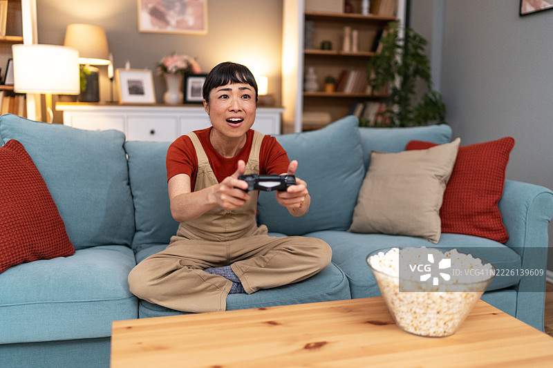 兴奋的女人在家沙发上玩电子游戏，旁边有爆米花图片素材