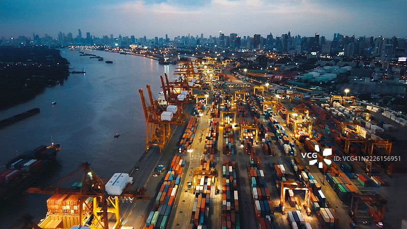 迷人的夜间航拍繁忙的货运港口，明亮的集装箱码头和货船展示了全球贸易和海洋物流，集装箱、大型货船和繁忙的起重机。图片素材