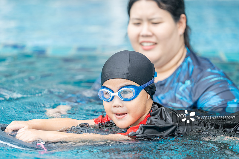 快乐的小运动员在母亲的陪伴下上游泳课 - 活泼的小男孩在蓝色泳池中与妈妈一起享受游泳的乐趣。家庭生活方式。图片素材