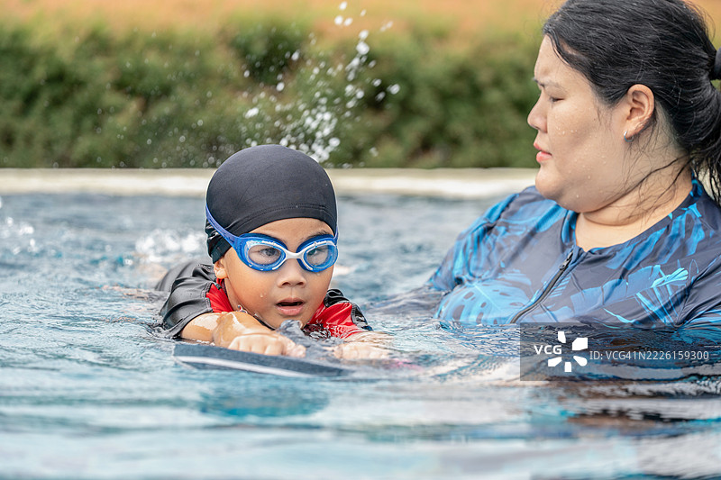 快乐的小运动员在母亲的陪伴下上游泳课 - 活泼的小男孩在蓝色泳池中与母亲一起快乐地游泳。家庭生活方式。图片素材