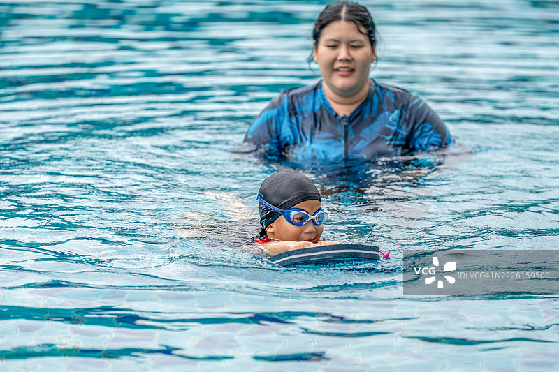 快乐的小运动员在母亲的陪伴下上游泳课 - 活泼的小男孩在蓝色泳池中享受游泳的乐趣，母亲抱着他。家庭生活方式。图片素材