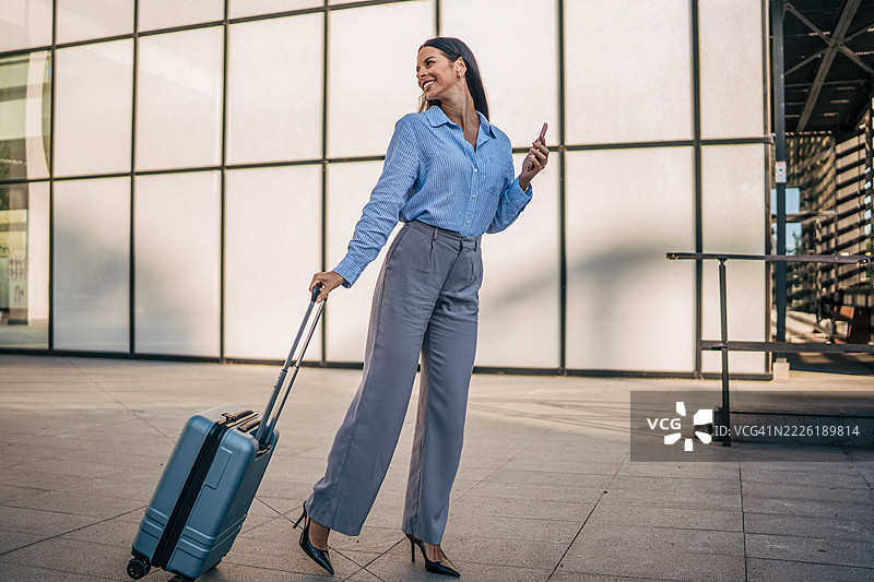 商务女性在机场走动，手提行李并使用智能手机图片素材