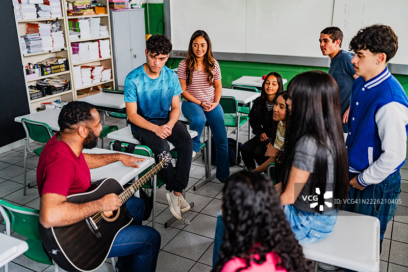 音乐老师在教室里给高中生上吉他课图片素材