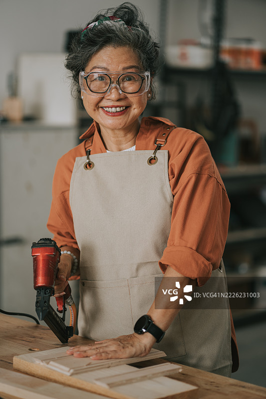 微笑着看向镜头的亚洲老年女性木匠在木工车间内的肖像图片素材