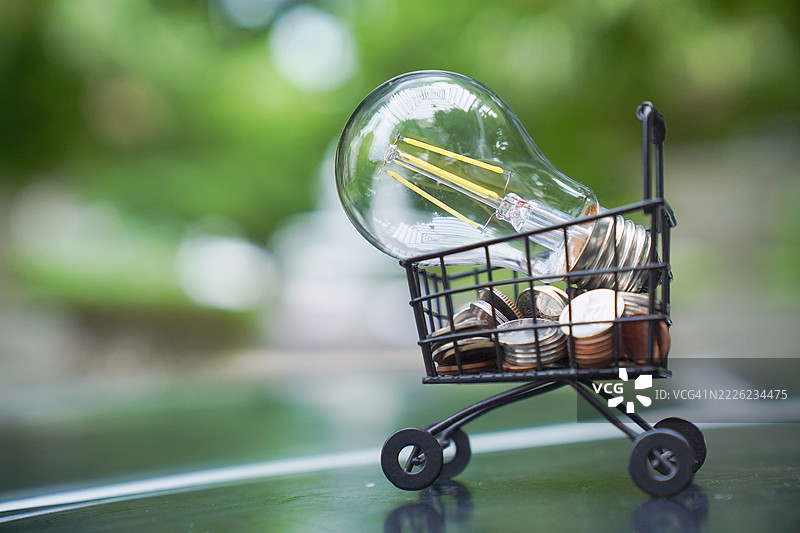 灯泡与堆叠的硬币和购物车。图片素材