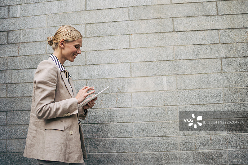 在灰色墙壁前使用数字平板的女商人图片素材