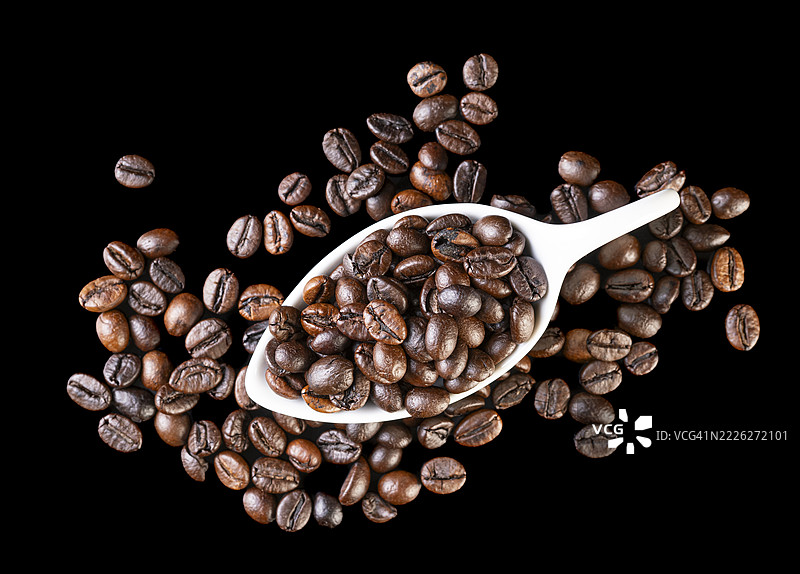 瓷勺中的烘焙咖啡豆，背景为光滑的黑色。图片素材