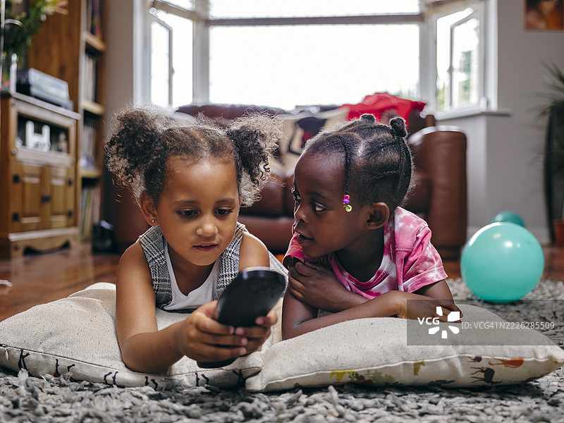 女孩们躺在地板上使用遥控器图片素材
