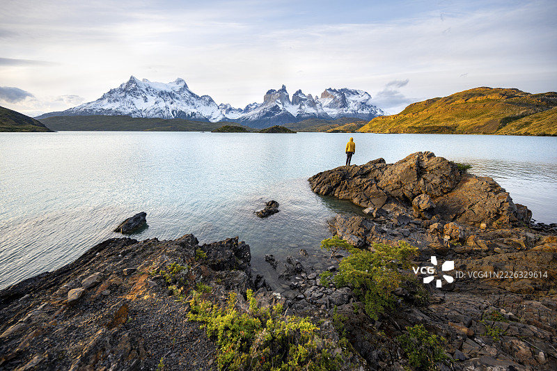 傍晚时分,年轻男子站在佩霍埃湖畔,背景是百内山脉,托雷斯·德·佩恩国家公园,智利图片素材