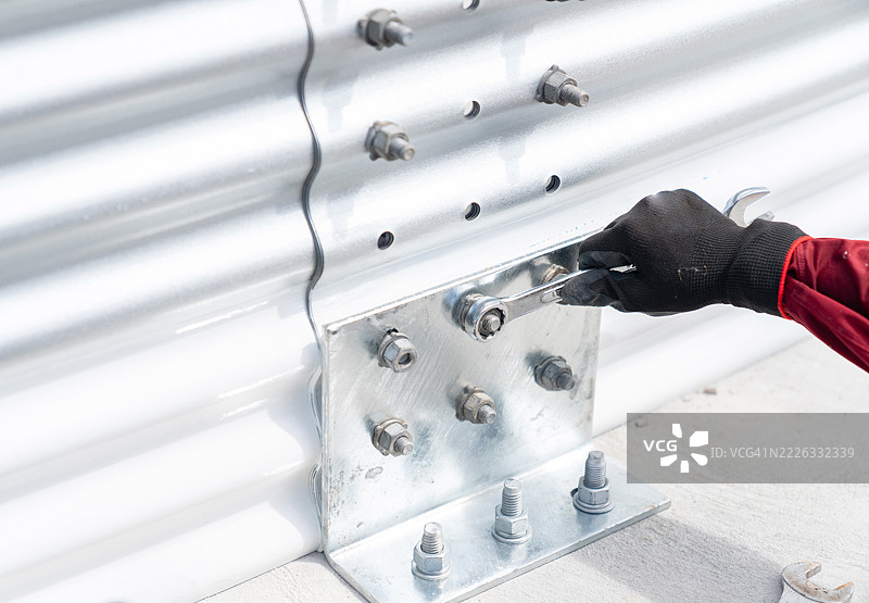 使用扳手拧紧固定在金属板墙上的螺栓。图片素材