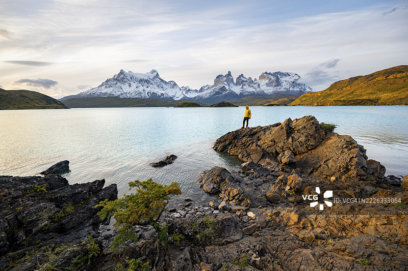 傍晚时分,年轻男子站在佩霍埃湖岸边,背景是百内角山脉,托雷斯·德·佩恩国家公园,智利。图片素材