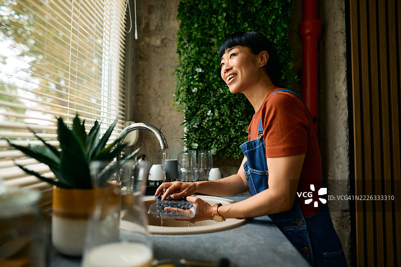 年轻女性在厨房水槽中清洗蓝莓，抬头微笑。图片素材