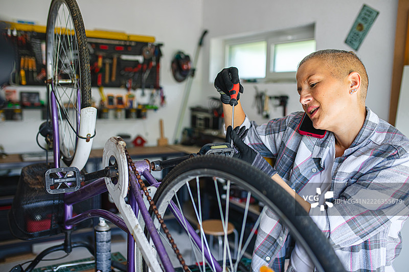 一位多任务处理的女性在修理自行车的同时打电话图片素材