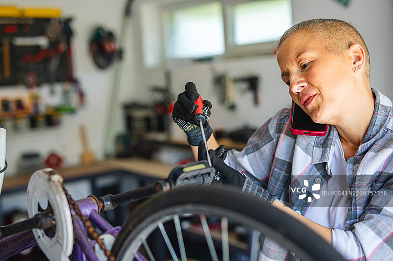 一位多任务处理的女性在修理自行车的同时打电话图片素材