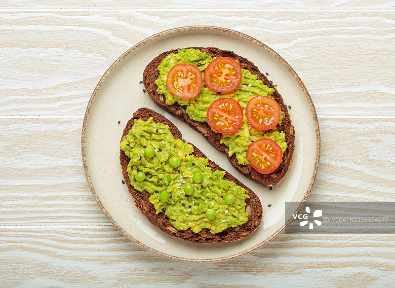 健康的鳄梨吐司，上面放有绿豌豆和樱桃番茄，搭配全麦黑麦面包图片素材