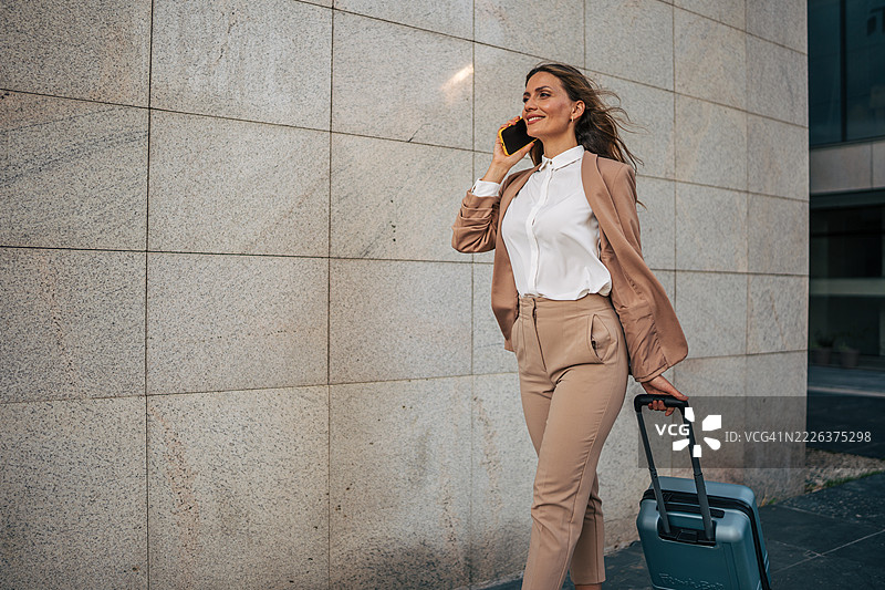商务女性一边走一边拖着行李箱，边打电话。图片素材