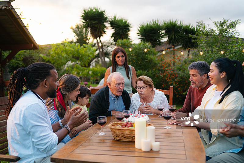 多代家庭在花园中欢庆祖父母的生日，周围有蛋糕、蜡烛和温暖的笑容图片素材