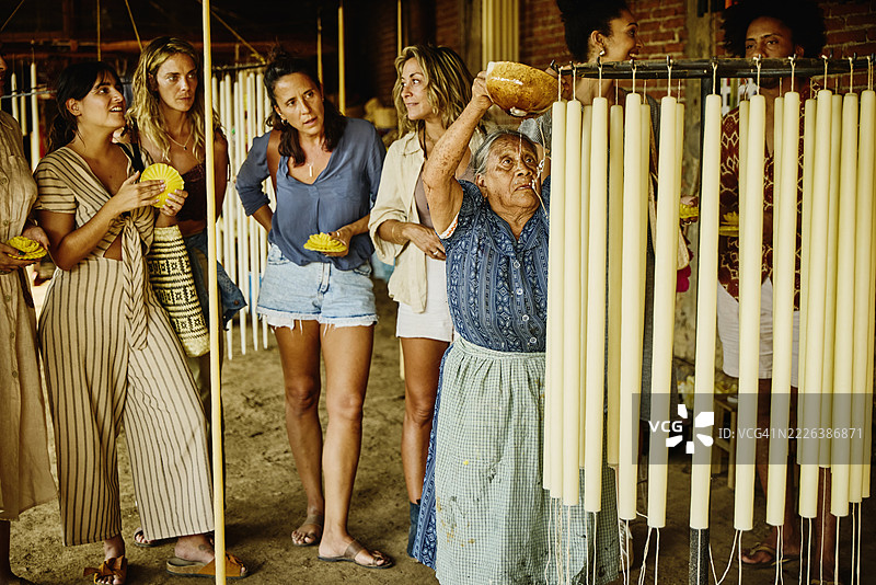 游客们在远景中观看蜡烛制造者为蜡烛添加一层蜡。图片素材