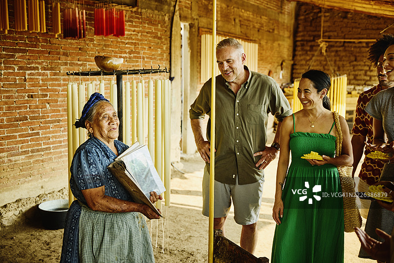 中景镜头，年长的工匠向游客展示她的蜡烛设计图片素材