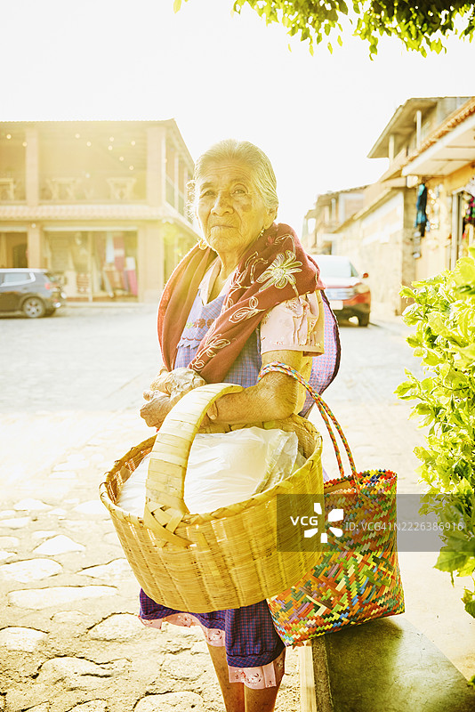 中景镜头的老年女性街头小吃摊贩提着篮子图片素材