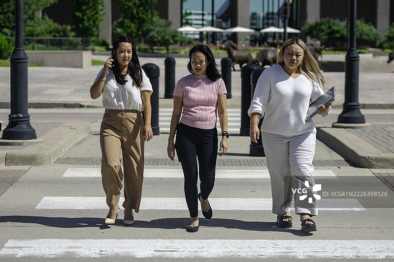 三位女性同事在一个美丽的日子里穿过马路，准备远程工作。图片素材