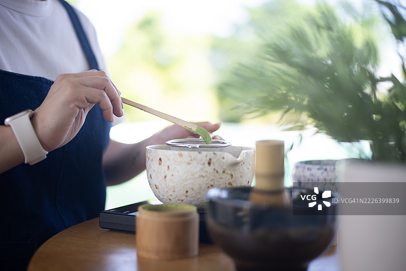女人的手在白色碗中用竹制茶筅搅拌抹茶绿茶。图片素材