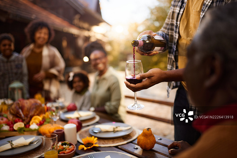 黑人男子在后院与家人共度感恩节午餐时倒酒的特写镜头。图片素材