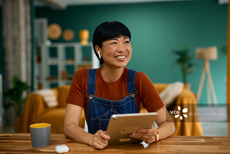 快乐的成熟亚洲女性在家中使用平板电脑听音乐图片素材
