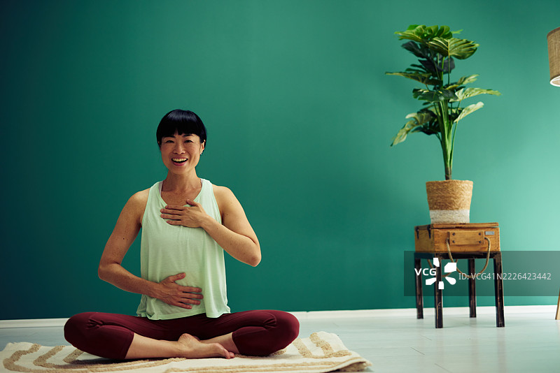 微笑的成熟的女性在家练习瑜伽和进行呼吸练习图片素材