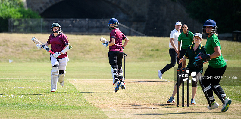 击球队在两条跑道之间奔跑，注视着球，守门员和外场队员准备将他们击出局。图片素材