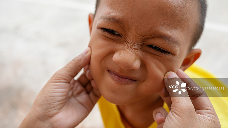 孩子顽皮地做着搞笑的表情，旁边有人轻轻捏着他们的脸颊，营造出轻松愉快的时刻。孩子穿着明亮的黄色衬衫，背景柔和模糊。图片素材