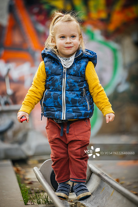 顽皮的男孩在游乐场的跑道上走，旁边是五彩缤纷的涂鸦墙图片素材