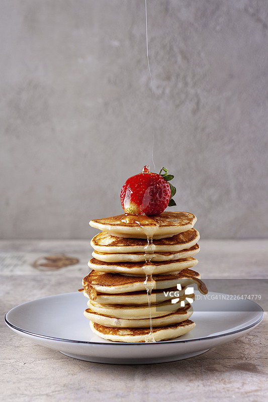 一丝细蜜缓缓流淌在草莓上，浇在一叠煎饼上。图片素材