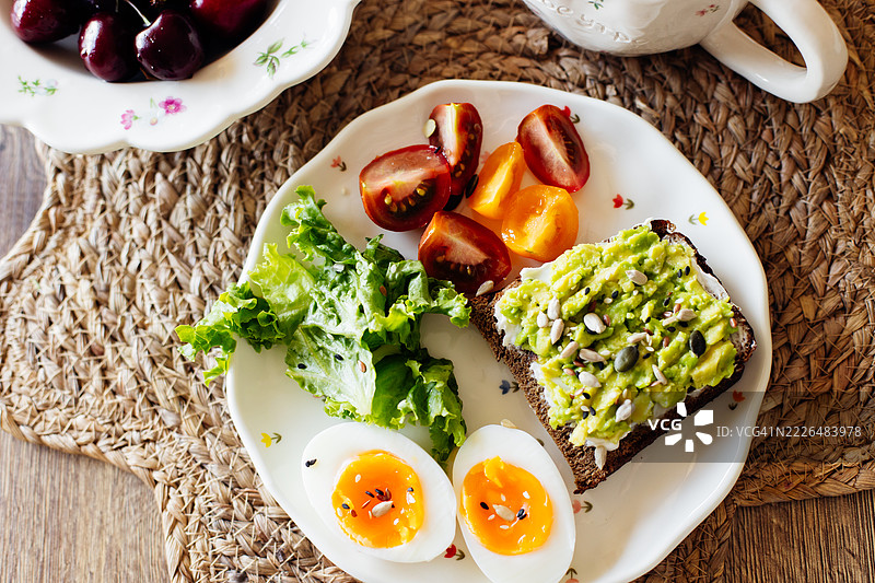鳄梨鸡蛋吐司。烤面包上放有鸡蛋、鳄梨、生菜和樱桃番茄。健康的小吃或早餐，摆放在木桌上。图片素材