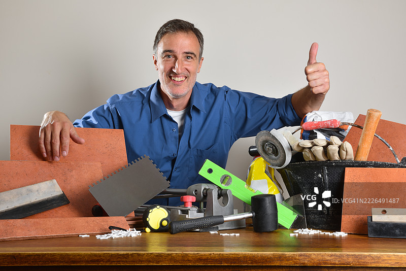 在西班牙，做瓷砖工的工人用“好的”手势展示木桌上的工具。图片素材