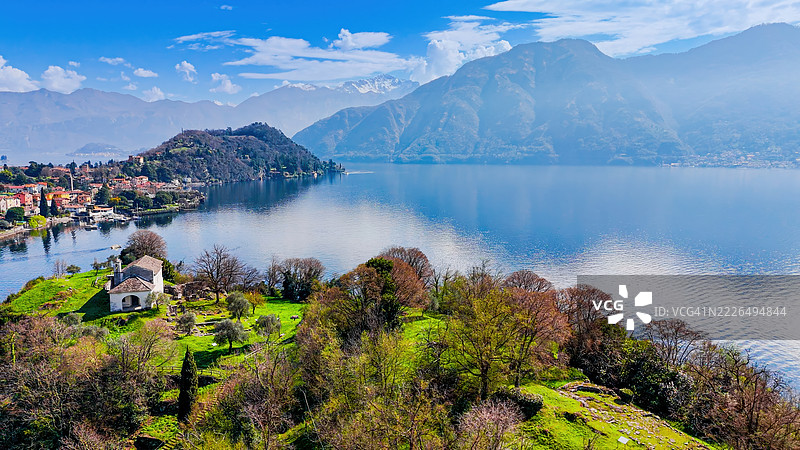 科莫湖上伊索拉科马奇纳的历史教堂鸟瞰图，周围是阿尔卑斯山的自然风光，传统宗教建筑与郁郁葱葱的绿地和宁静的水面相映成趣，意大利伦巴第的旅行、文化和遗产目的地。图片素材