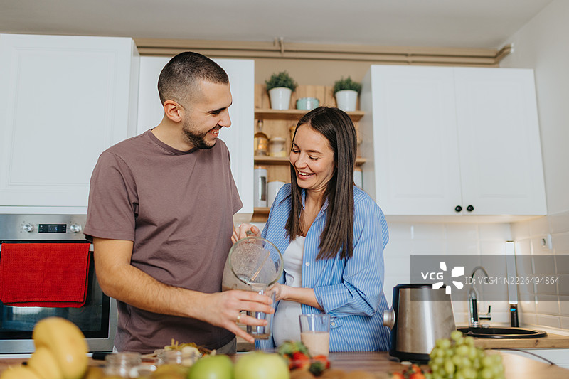 快乐的情侣在家准备健康的水果冰沙图片素材