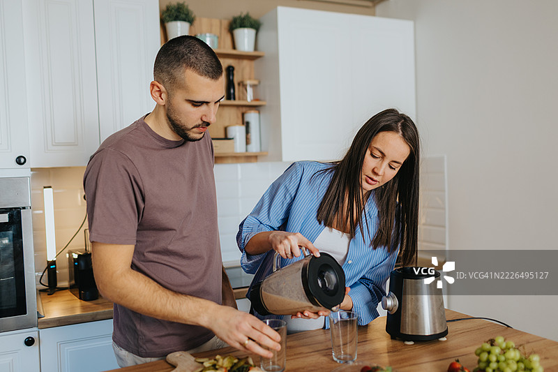 快乐的情侣在家准备健康的水果冰沙图片素材