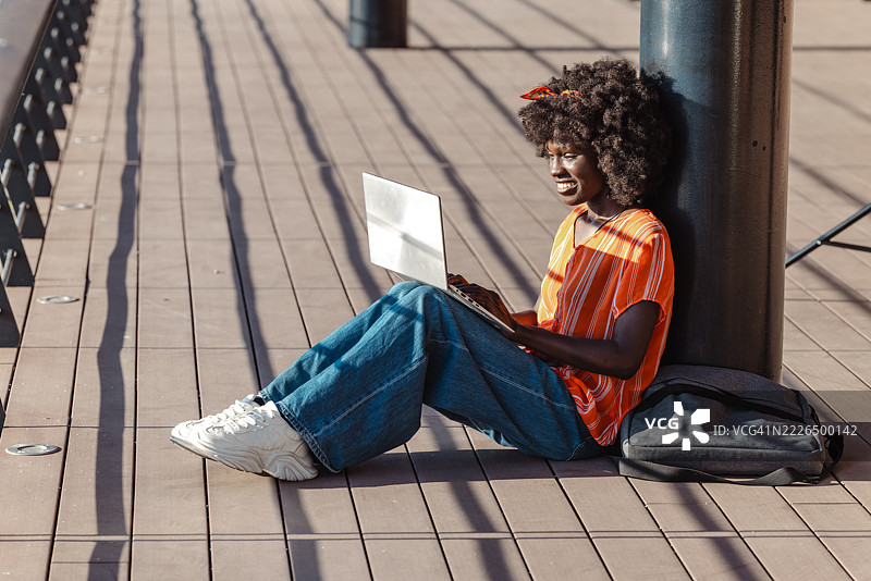 年轻女性在阳光明媚的日子里坐在户外使用笔记本电脑图片素材