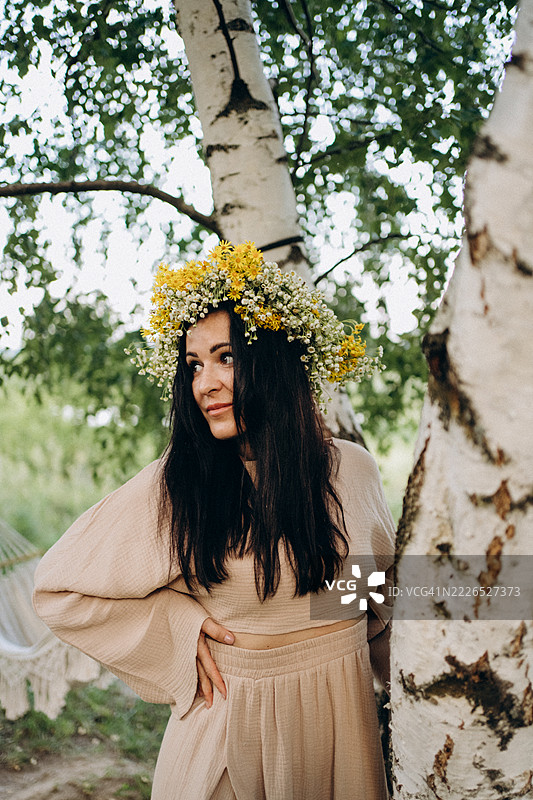 年轻女子戴着花冠，靠在夏天的白桦树上。图片素材