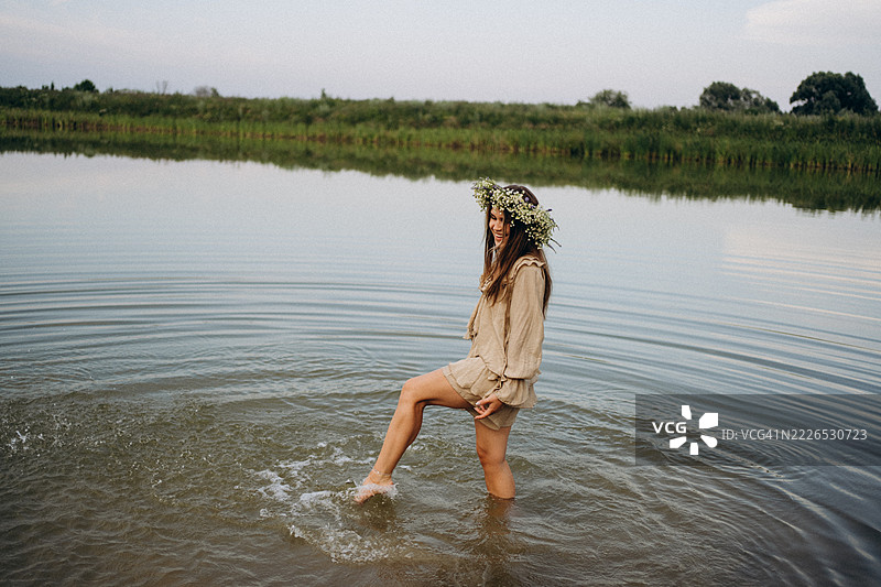 年轻女子在日落时分佩戴花冠走在湖中图片素材