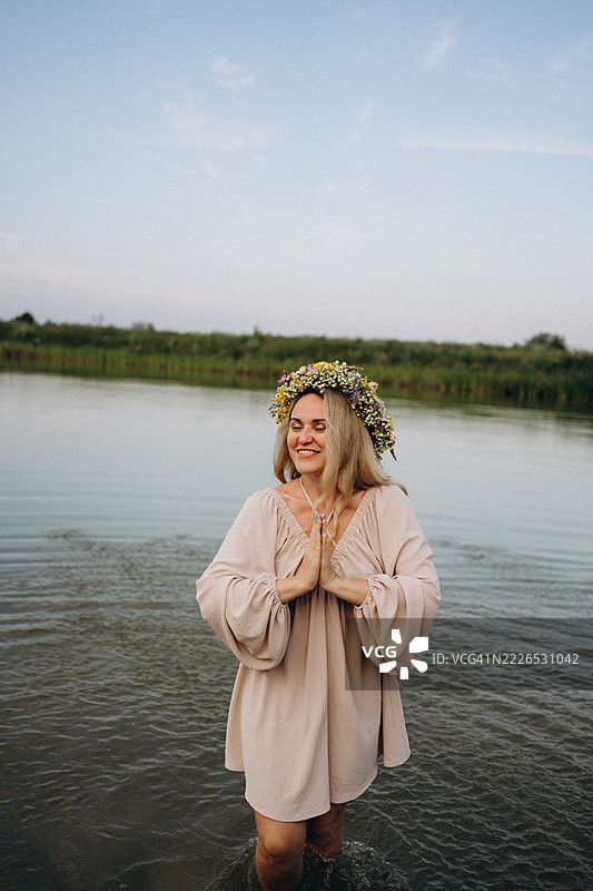 在日落时分，女人戴着花冠在湖中冥想图片素材