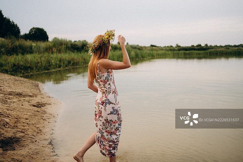 年轻女子戴着花冠走入日落时分的湖中图片素材