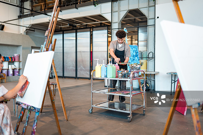 年轻的中东男性画家在明亮的工作室中调色板上混合颜料图片素材