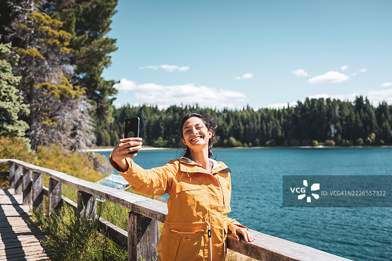 女人在巴塔哥尼亚的湖边木栈道上拍自拍，背景是美丽的风景图片素材