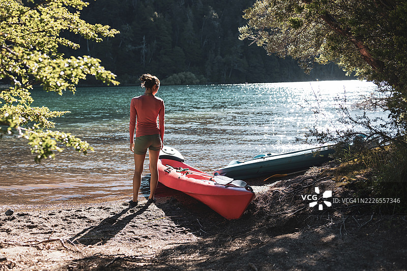 一位女性站在阿根廷巴塔哥尼亚的森林中，宁静湖边的皮划艇旁。图片素材