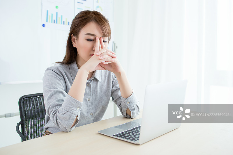坐在桌子前的女性，面前有笔记本电脑，看起来疲惫或压力很大图片素材