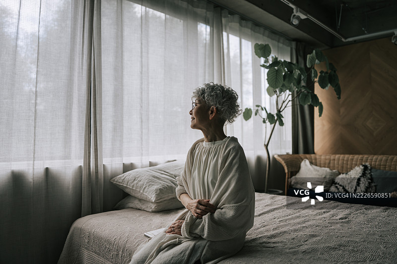 安静地坐在床上的日本老年女性，望着窗外。图片素材