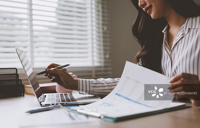 女商人在家办公室分析笔记本电脑和文件上的财务数据图片素材