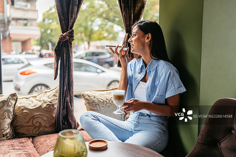 年轻女性在咖啡店里喝咖啡，同时在手机上发送语音消息图片素材